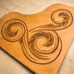 May include: A close-up of a piece of leather with a decorative design of three swirling patterns. The leather is a light brown colour and the design is embossed into the surface.