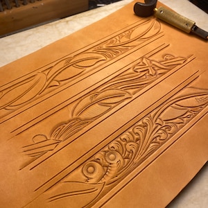 May include: A close-up of a piece of leather with three different floral designs carved into it. The leather is a light brown colour and the designs are intricate and detailed.