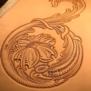 May include: A detailed floral design carved into a piece of leather. The design features a large flower with intricate details and swirling vines.