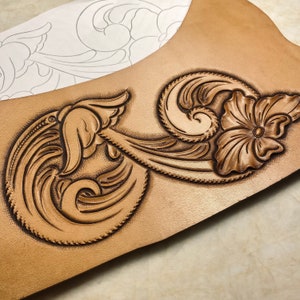 Puede incluir: Un primer plano de un proyecto de artesanía en cuero con un diseño floral detallado tallado en la superficie. El diseño presenta intrincados remolinos y una gran flor con un círculo central.