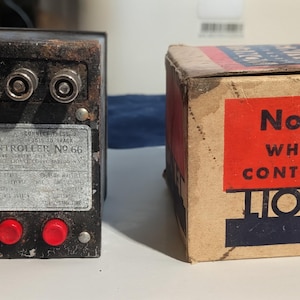 Puede incluir: Controlador de silbato Lionel No. 66 vintage y su caja original. El controlador es negro con detalles plateados y botones rojos. La caja es de color beige con una etiqueta roja que dice "No. 66 Whistle Controller Lionel."