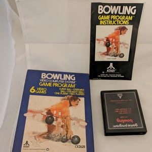 May include: A blue Atari game cartridge box with a picture of a person bowling. The box is labeled "Bowling Video Computer System Game Program" and features the Atari logo. The cartridge is black with red text that reads "Bowling Game Program".