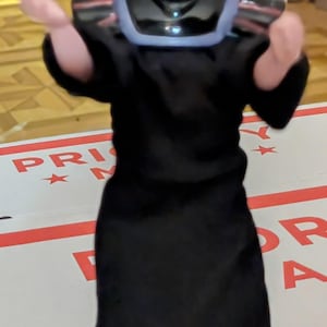 May include: A black and blue plastic toy figure of a man wearing a black robe and a blue and black hat. The figure is holding out its left arm and has a stern expression on its face.