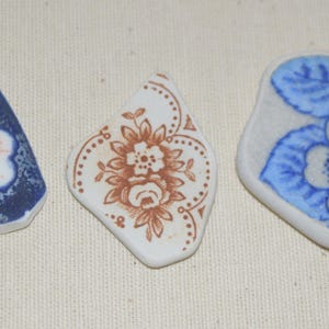 May include: Three pieces of vintage ceramic with floral designs. One piece features a blue and white flower with orange accents, another has a brown floral pattern, and the third displays a blue and white floral design.