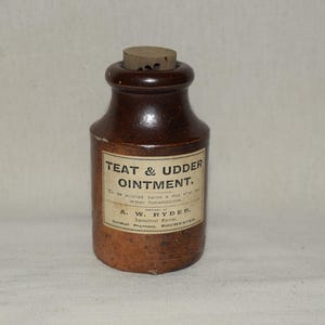 May include: A brown ceramic bottle with a cork stopper, labelled "TEAT & UDDER OINTMENT." The label also includes application instructions and the name A. W. Ryder, Agricultural Chemist, Guildhall Pharmacy, Rochester.