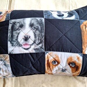 May include: Black quilted cushion with a patchwork design featuring images of different dog breeds. The dog faces are in squares, set against a black background with diamond stitching. The cushion has a black border.