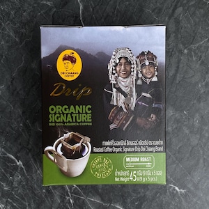 Puede incluir: Una caja de café Doi Chaang Organic Signature Drip. La caja presenta el logotipo de la marca, las palabras "Drip Organic Signature" y una ilustración de dos personas. También incluye el texto "SHB 100% Arabica Coffee".