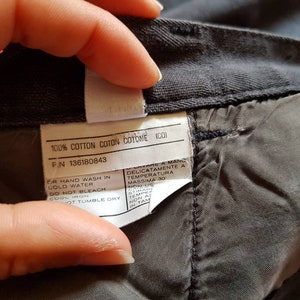 May include: A close-up of a grey cotton fabric label with care instructions. The label includes the text "100% Cotton Coton Cotome (CO)" and "F.N 136180843". The care instructions include "Or hand wash in cold water", "Do not bleach", "Cool iron", and "Hot tumble dry".