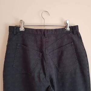 May include: Black high-waisted jeans with a classic five-pocket design. The jeans are hanging on a silver hanger.