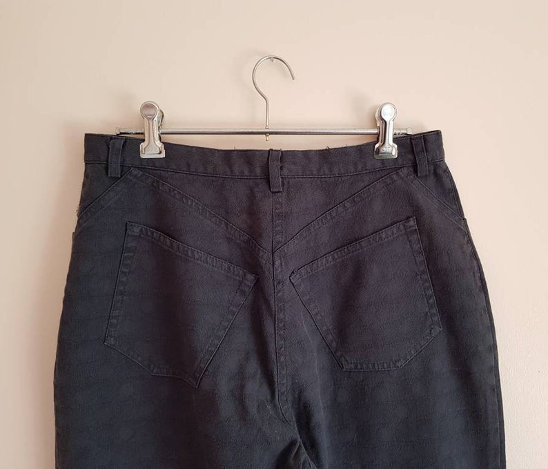 May include: Black high-waisted jeans with a classic five-pocket design. The jeans are hanging on a silver hanger.