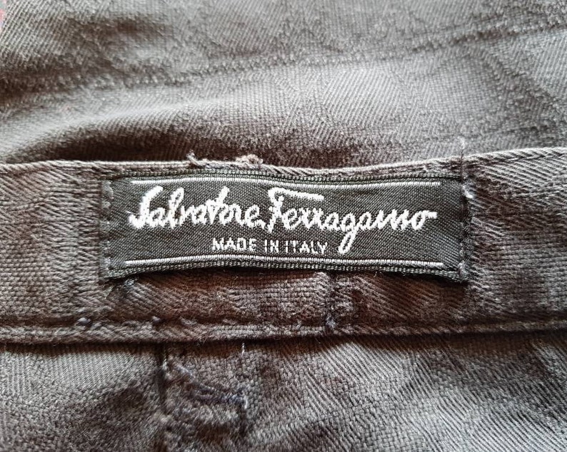 May include: A black fabric label with white text that reads "Salvatore Ferragamo Made in Italy".