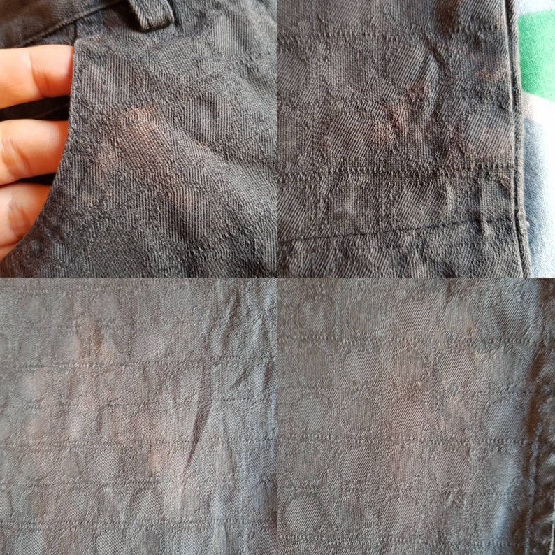 May include: Close-up of a dark grey fabric with a subtle textured pattern. The fabric has a slightly worn look, with some faint lines and creases.