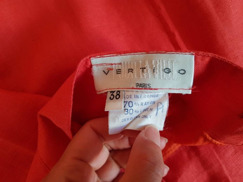 May include: A red linen blend skirt with a white label that reads "VERTIGO PARIS" and size 38. The label also includes care instructions: "Made in France, 70% Rayon, 30% Linen, Dry Clean Only."