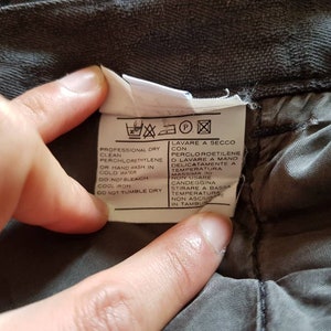 May include: A white care label with black text and symbols. The text reads "Professional dry clean perchlorethylene or hand wash in cold water. Do not bleach. Cool iron. Do not tumble dry." The text also reads "Lavare a secco con percloroetilene o lavare a mano delicatamente a temperatura massima 30. Non usare candeggina. Stirare a bassa temperatura. Non asciugare in tamburo."