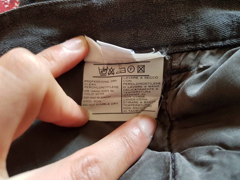 May include: A white care label with black text and symbols. The text reads "Professional dry clean perchlorethylene or hand wash in cold water. Do not bleach. Cool iron. Do not tumble dry." The text also reads "Lavare a secco con percloroetilene o lavare a mano delicatamente a temperatura massima 30. Non usare candeggina. Stirare a bassa temperatura. Non asciugare in tamburo."