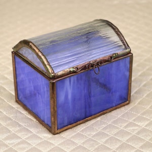 Może przedstawiać: Mała, niebieska szklana skrzynka z miedzianą pokrywą i zawiasem. Skrzynka ma przezroczysty szklany wierzch i jest ozdobiona wirującym wzorem.