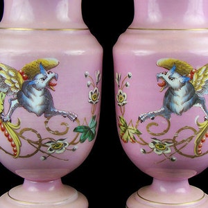 May include: A pair of pink porcelain vases with gold accents and hand-painted winged creatures. The vases have a delicate floral design and are in excellent condition.
