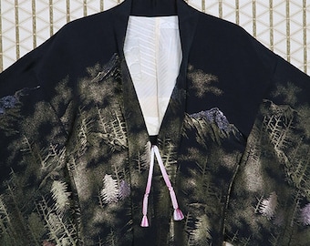Könnte beinhalten: Ein schwarzer Seidenkimono mit einem goldenen und grünen Berg- und Waldmotiv. Der Kimono hat eine rosa und goldene Krawatte.