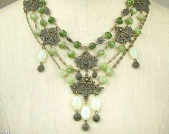May include: A multi-strand necklace featuring green and white beads with intricate metal embellishments. The necklace has a cascading design with a large pendant at the centre.