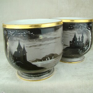 Puede incluir: Dos tazas de porcelana en blanco y negro con ribete dorado. Cada taza presenta una silueta de un castillo y un paisaje iluminado por la luna.