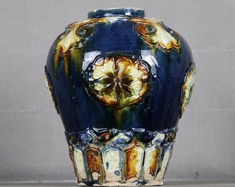 May include: A blue and yellow ceramic vase with intricate floral designs. The vase has a rounded body and a narrow neck.