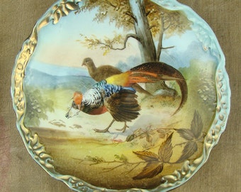 Plato antiguo de porcelana pintado a mano con aves de caza en un paisaje, firmado por un artista, siglo XIX, con detalles dorados y figuras de animales.