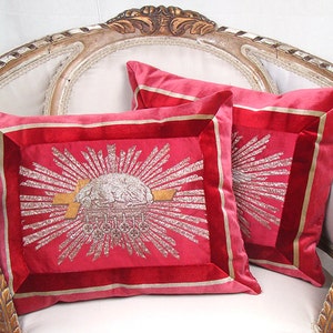 May include: Two red velvet throw pillows with gold and silver embroidery. The pillows feature a sunburst design with a central image of a crown.
