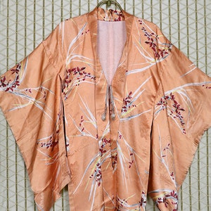 May include: A peach-colored Japanese kimono with a floral pattern of white, red, and yellow flowers. The kimono is made of silk and has a traditional design.