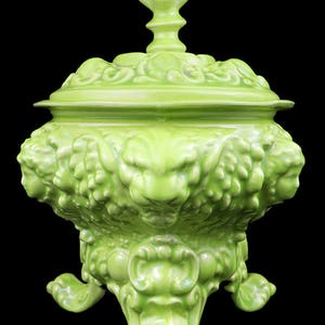 May include: A green ceramic lidded bowl with intricate floral and scrollwork designs. The bowl has three legs and a decorative finial on the lid.