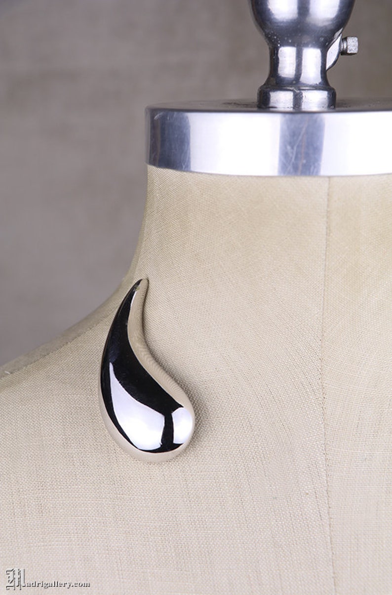 May include: A silver-toned, abstract, teardrop-shaped brooch.