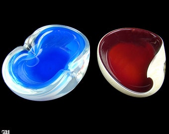 May include: Two glass ashtrays, one blue and one red. The blue ashtray has a white rim and a swirl design. The red ashtray has a silver rim.