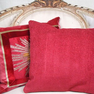 May include: Two decorative pillows on a white couch. One pillow is red with a textured surface. The other pillow is red with a gold embroidered design.
