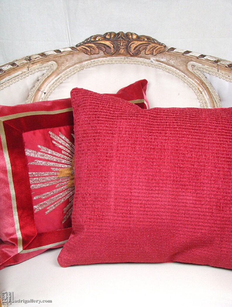 May include: Two decorative pillows on a white couch. One pillow is red with a textured surface. The other pillow is red with a gold embroidered design.