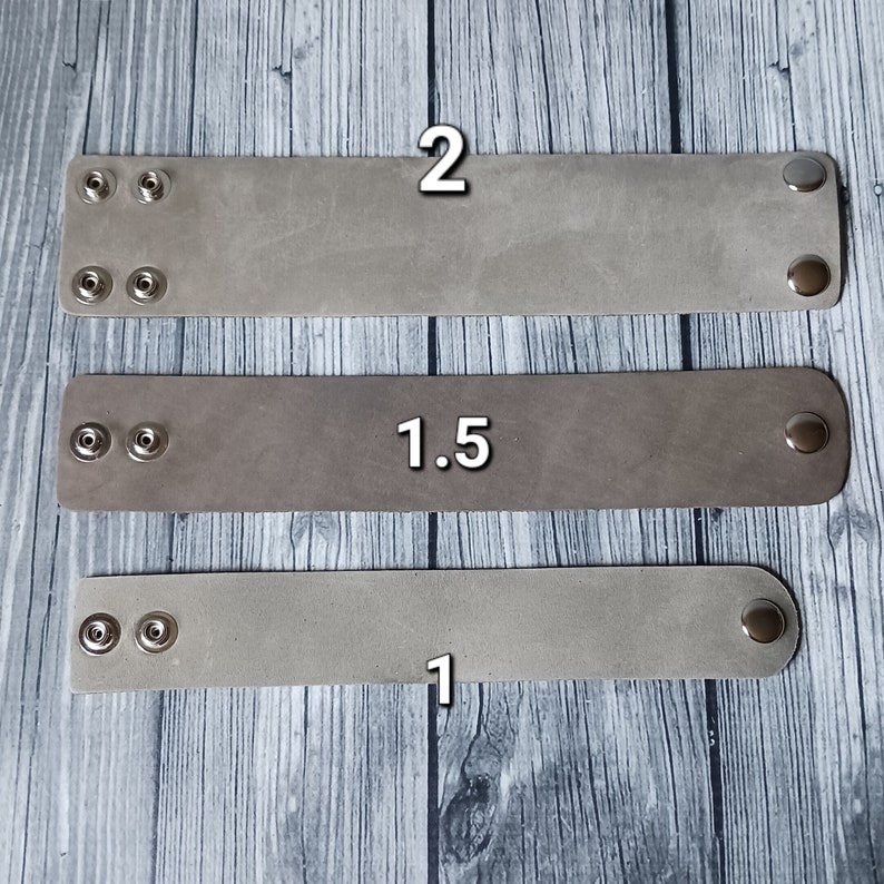May include: Three rectangular light grey leather wristbands of varying widths, labelled 2, 1.5, and 1. Each band features two silver-toned metal snap fasteners on one end and a single matching snap fastener on the opposite end for closure.