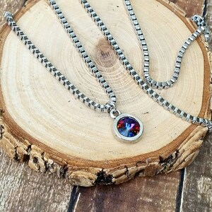 May include: A silver chain necklace with a round pendant featuring a multi-colored iridescent gemstone.