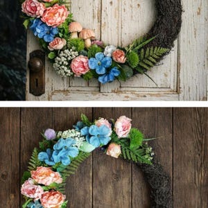 May include: A circular wreath featuring a dark brown twig base adorned with blue and pink flowers, green fern fronds, small white clusters, and light brown mushroom figures. The floral arrangement is concentrated along the left side of the wreath.