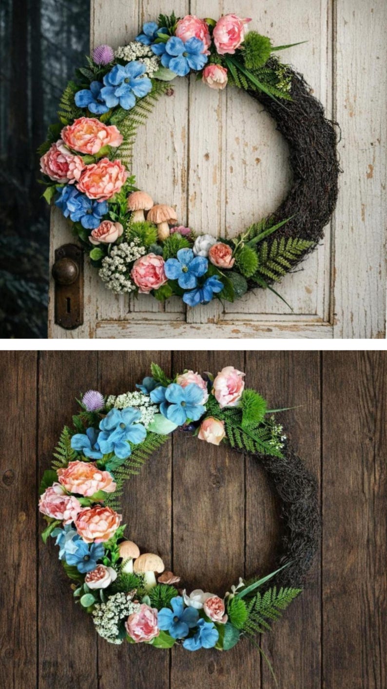 May include: A circular wreath featuring a dark brown twig base adorned with blue and pink flowers, green fern fronds, small white clusters, and light brown mushroom figures. The floral arrangement is concentrated along the left side of the wreath.