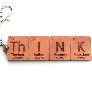 Peut inclure: Porte-clés en bois avec le mot "THINK" orthographié à l'aide des symboles chimiques et des noms des éléments Thorium, Iode, Azote et Potassium.
