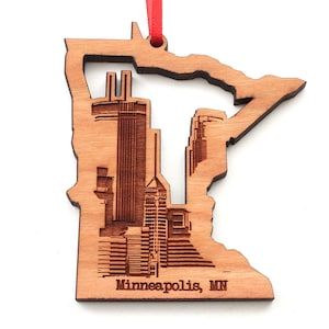Może przedstawiać: Drewniana ozdoba w kształcie stanu Minnesota z laserowo wyciętym szczegółowym wzorem panoramy Minneapolis. Ozdoba jest brązowa i ma napis "Minneapolis, MN" na dole.