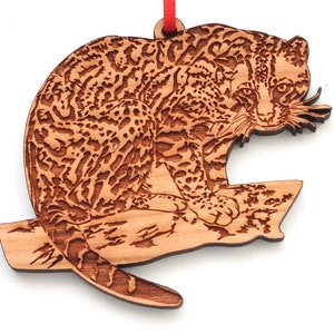 Op de afbeelding: Houten ornament van een gevlekte ocelot die op een tak zit. De ocelot is gedetailleerd gesneden en heeft een realistisch uiterlijk.