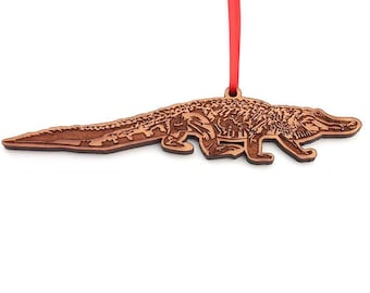 May include: A wooden alligator ornament with a detailed design, hanging from a red ribbon.