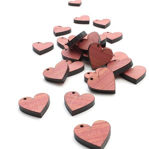 May include: A pile of small wooden hearts in a reddish-brown color with black edges. The hearts are scattered on a white background.