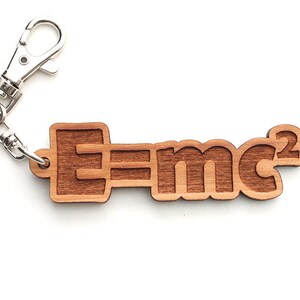 Puede incluir: Un llavero de madera con una cadena y un cierre de metal plateado. El llavero presenta la ecuación "E=mc²" en una fuente estilizada.