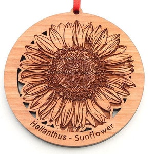 May include: A wooden ornament featuring a detailed laser-cut design of a sunflower. The ornament is round and has a red ribbon attached to the top. The text "Helianthus - Sunflower" is inscribed at the bottom.