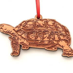 May include: A wooden ornament shaped like a tortoise. The ornament is brown and has a detailed design of the tortoise's shell.