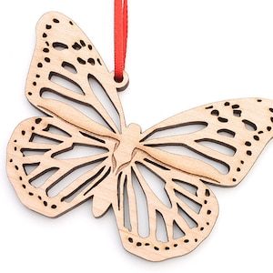 May include: A wooden butterfly ornament with intricate cutouts, painted in a natural wood color. The ornament is attached to a red ribbon.