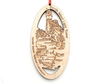 Könnte beinhalten: Ein ovaler Holzschmuck mit einem Laser-Cut-Design des Devils Island Leuchtturms im Apostle Islands National Lakeshore. Der Anhänger ist aus hellbraunem Holz gefertigt und hat ein rotes Band, das oben befestigt ist.