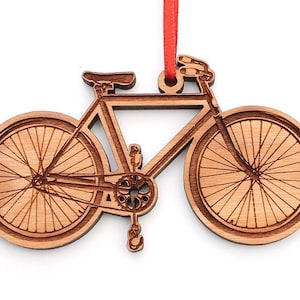 May include: Wooden ornament shaped like a bicycle with brown wood grain. The ornament has a red ribbon attached to the top.