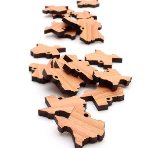 May include: A pile of wooden Texas state outline ornaments. The ornaments are light brown with a dark brown outline.