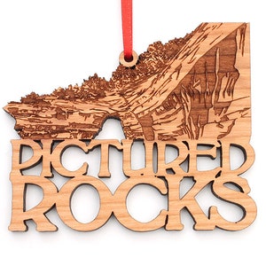 May include: A wooden ornament featuring a detailed laser-engraved image of Pictured Rocks National Lakeshore in Michigan. The ornament is brown and has the words "Pictured Rocks" cut out below the image.